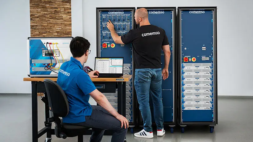 Zwei comemso-Ingenieure konfigurieren im Labor ein Battery Cell Simulator-Prüfsystem