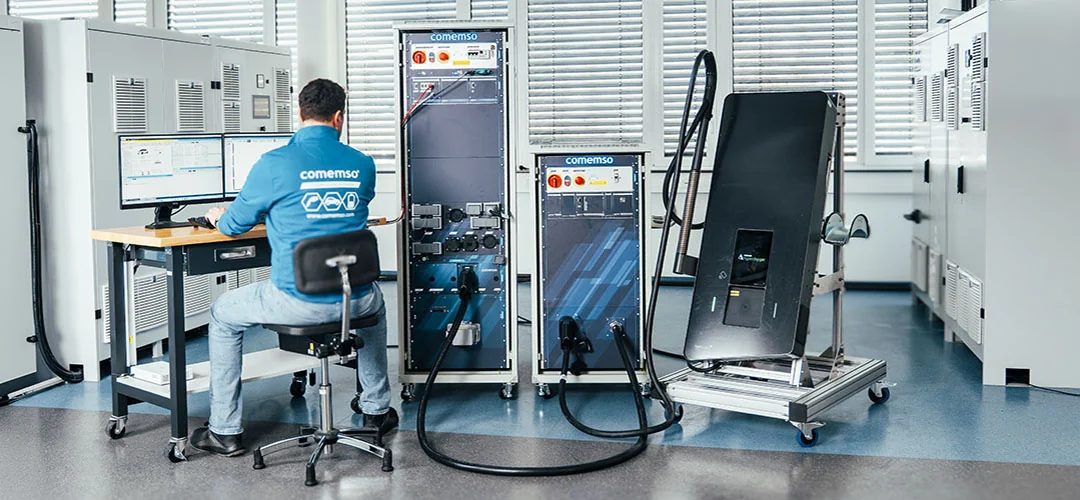 A comemso engineer at an EVCA test system with a charging station connected in the lab