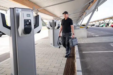 Ein Techniker trägt Easy Chester Micro im geschlossenen Koffer und ein Ladekabel zu einer AC-Ladestation.